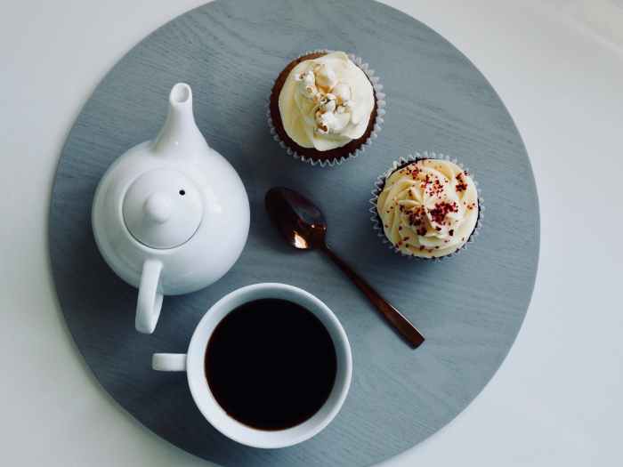 white ceramic cup and teapot with cupcakes